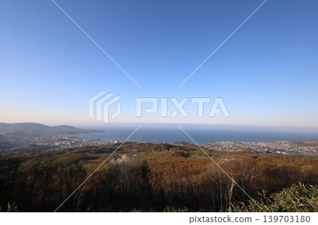 In early May, in Hokkaido, a view of Otaru, Hokkaido, from the observation point on Mount Kenashi, overlooking the harbor and Ishikari Bay, against a blue sky and evening twilight. In early May, in Hokkaido, a view of Otaru, Hokkaido, from the observation point on Mount Kenashi, overlooking the harbor and Ishikari Bay, against a blue sky and evening twilight. 139703180