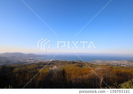 In early May, in Hokkaido, a view of Otaru, Hokkaido, from the observation point on Mount Kenashi, overlooking the harbor and Ishikari Bay, against a blue sky and evening twilight. In early May, in Hokkaido, a view of Otaru, Hokkaido, from the observation point on Mount Kenashi, overlooking the harbor and Ishikari Bay, against a blue sky and evening twilight. 139703181