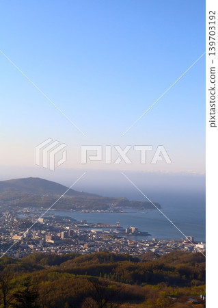 In early May, in Hokkaido, a view of Otaru, Hokkaido, from the observation point on Mount Kenashi, overlooking the harbor and Ishikari Bay, against a blue sky and evening twilight. 139703192