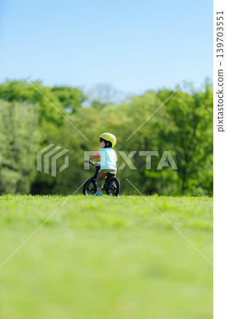 A 2-year-old boy riding a balance bike in the park. A 2-year-old boy riding a balance bike in the park. 139703551