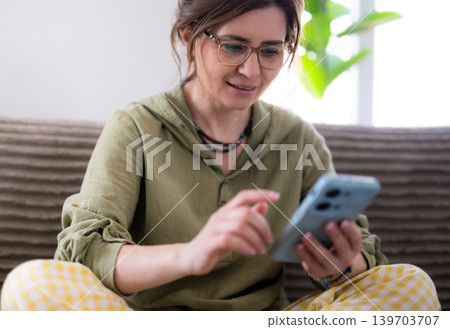 Young Woman Surfing The Internet On Smartphone On A Couch In A Light Room Young Woman Surfing The Internet On Smartphone On A Couch In A Light Room 139703707