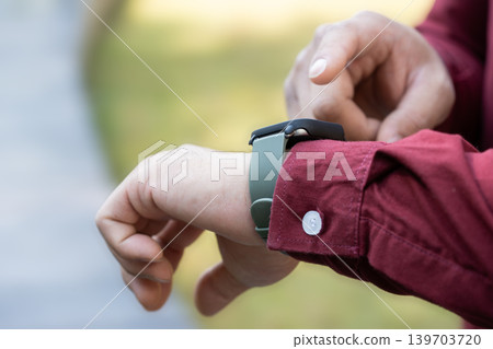 The close up of a man wearing a smartwatch on his left wrist and using this device outside. Electric gadget and a user shot on blurry background. The close up of a man wearing a smartwatch on his left wrist and using this device outside. Electric gadget and a user shot on blurry background. 139703720