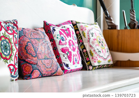 Many square pillow with colorful floral geometric pattern are arranged orderly on the white wooden sofa. 139703723