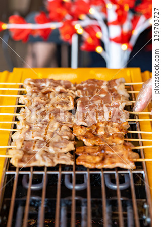 The shot of a cook grill Moo Ping or grilled pork skewers in Thai style on the yellow electric barbeque grill at the restaurant. The shot of a cook grill Moo Ping or grilled pork skewers in Thai style on the yellow electric barbeque grill at the restaurant. 139703727