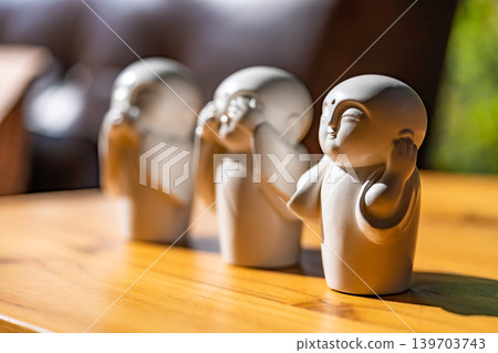 The white ceramic statue of three little monk See, Hear, Speak no evil set for home decoration placed on the wooden table over the black wall. 139703743