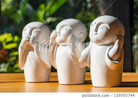The white ceramic statue of three little monk See, Hear, Speak no evil set for home decoration placed on the wooden table over the black wall. 139703744