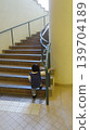 The back view of a girl trying to climb the stairs of a building, holding onto the handrail. 139704189