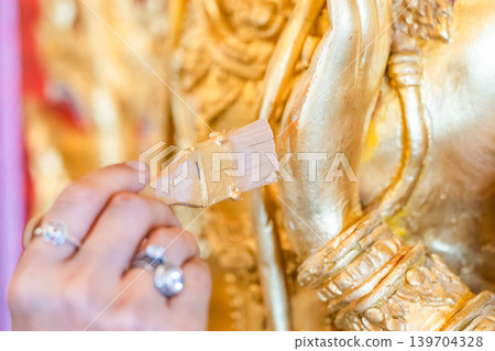 Hands painting gold on deity relief temple wall small brush detail work sacred restoration conservation protection. Hands painting gold on deity relief temple wall small brush detail work sacred restoration conservation protection. 139704328