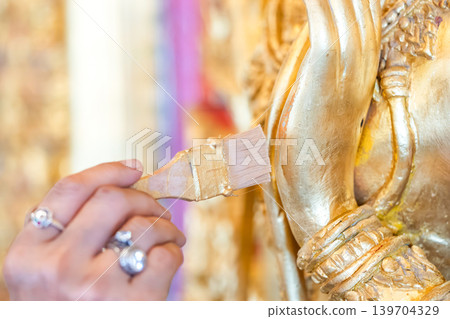 Hands painting gold on deity relief temple wall small brush detail work sacred restoration conservation protection. Hands painting gold on deity relief temple wall small brush detail work sacred restoration conservation protection. 139704329