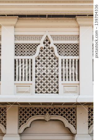 Elegant white Thai architectural facade featuring symmetrical lattice patterns and traditional ornamental details in minimalist temple design style. Elegant white Thai architectural facade featuring symmetrical lattice patterns and traditional ornamental details in minimalist temple design style. 139704336