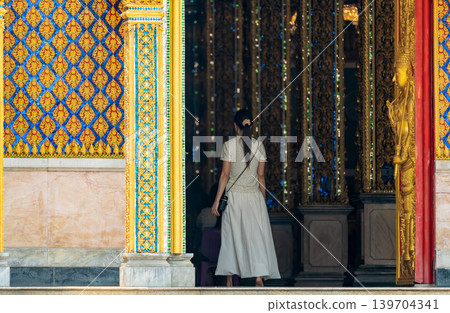 Long perspective corridor inside a Thai temple featuring golden frames, colorful columns, and symmetrical Buddhist architectural details. 139704341