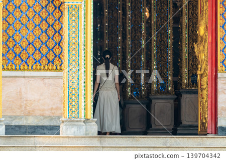 Long perspective corridor inside a Thai temple featuring golden frames, colorful columns, and symmetrical Buddhist architectural details. 139704342