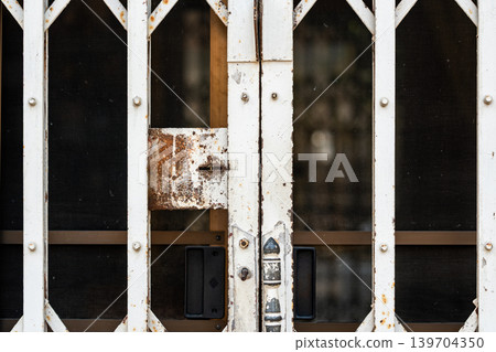 Old rusty folding metal security gate with locked entrance and geometric lattice pattern on urban building exterior. Old rusty folding metal security gate with locked entrance and geometric lattice pattern on urban building exterior. 139704350