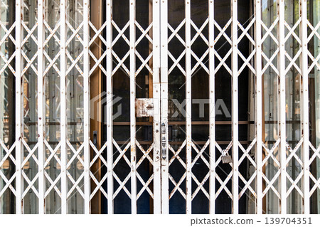 Old rusty folding metal security gate with locked entrance and geometric lattice pattern on urban building exterior. Old rusty folding metal security gate with locked entrance and geometric lattice pattern on urban building exterior. 139704351