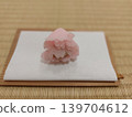 A light pink Japanese sweet is placed on a piece of paper. 139704612