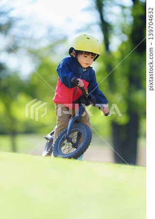 A 2-year-old boy practices riding a balance bike on an off-road course. A 2-year-old boy practices riding a balance bike on an off-road course. 139704632