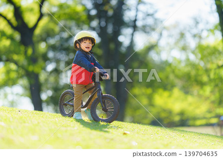 A 2-year-old boy practices riding a balance bike on an off-road course. 139704635