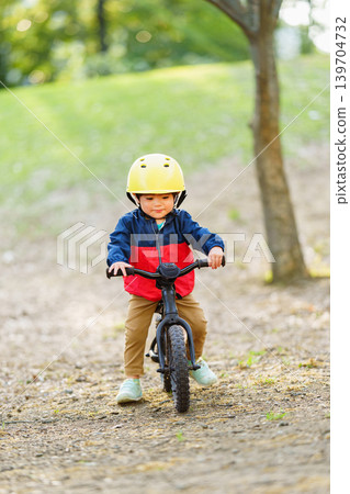 A 2-year-old boy practices riding a balance bike on an off-road course. A 2-year-old boy practices riding a balance bike on an off-road course. 139704732