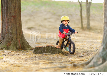 A 2-year-old boy practices riding a balance bike on an off-road course. A 2-year-old boy practices riding a balance bike on an off-road course. 139704733