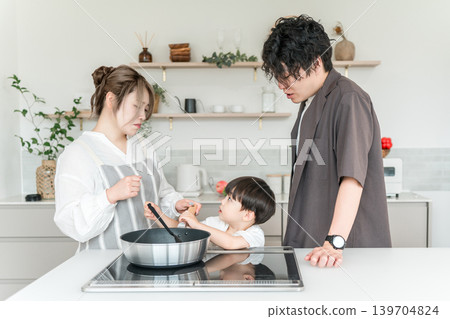 A little boy is playing pranks on his mom while she's cooking in the kitchen. A little boy is playing pranks on his mom while she's cooking in the kitchen. 139704824