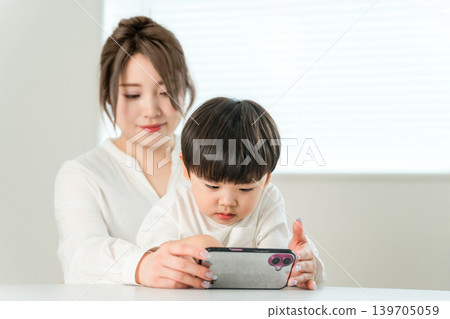 A boy watching anime and videos on his smartphone while sitting on his mom's lap. 139705059