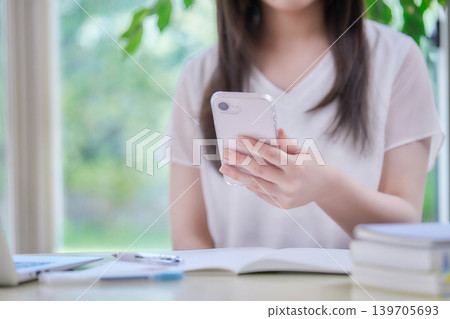 A young woman studying while looking at her smartphone. A young woman studying while looking at her smartphone. 139705693