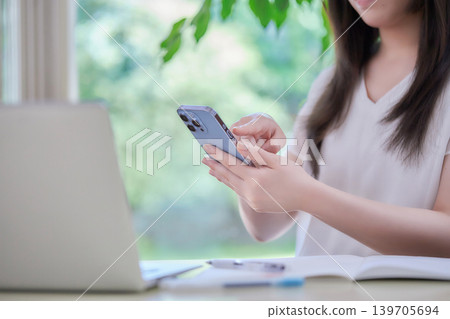 一位年輕女子一邊學習一邊看手機。 139705694