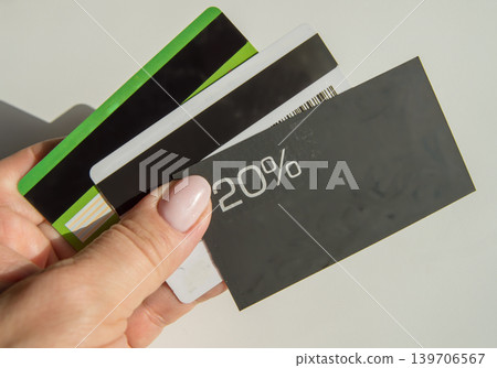 A man's hand holding a discount card with a 20 percent discount and a copy of the place and several plastic bank cards, the concept of saving finances A man's hand holding a discount card with a 20 percent discount and a copy of the place and several plastic bank cards, the concept of saving finances 139706567