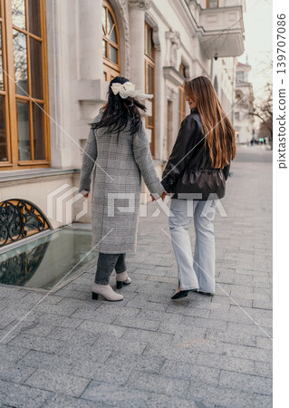 Women friends walking together along city sidewalk past classical building architecture on a sunny day during travel trip Women friends walking together along city sidewalk past classical building architecture on a sunny day during travel trip 139707086