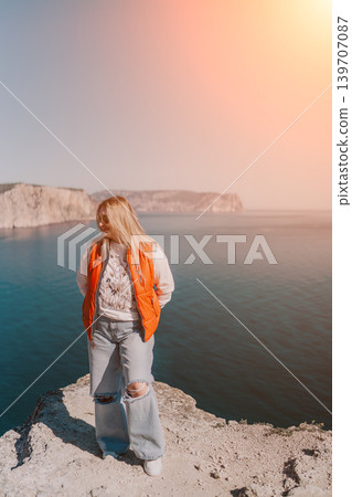 Woman cliff ocean standing on a rocky peak overlooking the blue sea and distant mountains during golden hour 139707087