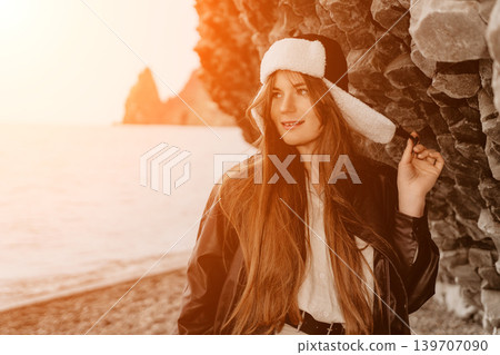Woman winter sunset stands by the sea wearing an ushanka hat and leather jacket enjoying the warm golden hour light Woman winter sunset stands by the sea wearing an ushanka hat and leather jacket enjoying the warm golden hour light 139707090