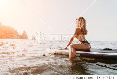 Woman Paddle Board Ocean - A woman sits on a paddle board in the ocean, looking out at the horizon. 139707183