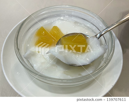 Almond tofu topped with yellow peaches, served in a glass bowl. Almond tofu topped with yellow peaches, served in a glass bowl. 139707611