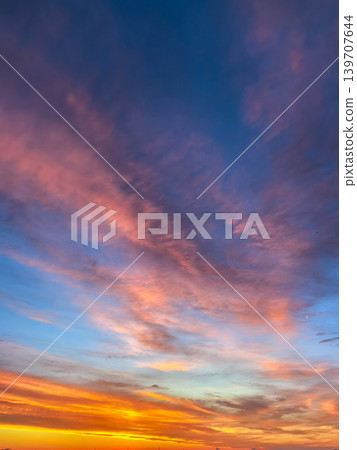 Bright sunset sky featuring flowing pink and orange clouds across a blue evening background. Scenic outdoor atmosphere with dramatic cloud movement and warm tones. Bright sunset sky featuring flowing pink and orange clouds across a blue evening background. Scenic outdoor atmosphere with dramatic cloud movement and warm tones. 139707644