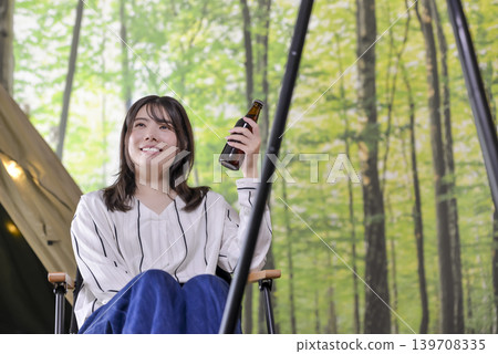 一位微笑的年輕女子在露營地享用啤酒。 139708335
