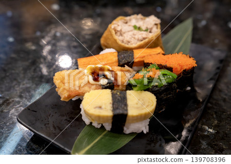 Assorted Japanese sushi platter with tamago nigiri, kani, tobiko gunkan, and seaweed salad on a black plate. Fresh seafood and rice served for a gourmet dining experience in a restaurant setting. Assorted Japanese sushi platter with tamago nigiri, kani, tobiko gunkan, and seaweed salad on a black plate. Fresh seafood and rice served for a gourmet dining experience in a restaurant setting. 139708396