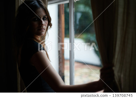Woman, portrait and window at night in dark room in stress, anxiety or mental health for lonely indoor home. Young female person standing by glass at house by curtains in neighborhood apartment Woman, portrait and window at night in dark room in stress, anxiety or mental health for lonely indoor home. Young female person standing by glass at house by curtains in neighborhood apartment 139708745