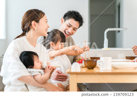 Girl and family practicing using chopsticks while playing house at the dinner table, Family Girl and family practicing using chopsticks while playing house at the dinner table, Family 139709123