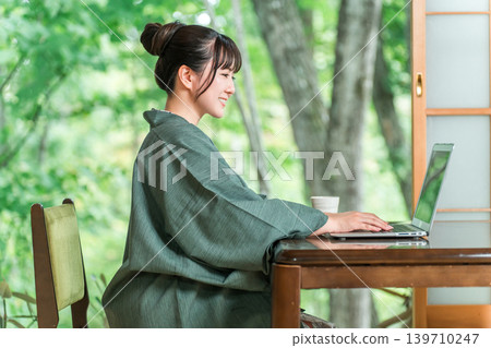 A woman in a yukata working on a computer in a room at a hot spring inn A woman in a yukata working on a computer in a room at a hot spring inn 139710247