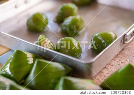 Traditional Thai Khanom Tian dessert prepared green dough banana leaf wrapping showing homemade festive sweet preparation Traditional Thai Khanom Tian dessert prepared green dough banana leaf wrapping showing homemade festive sweet preparation 139710368