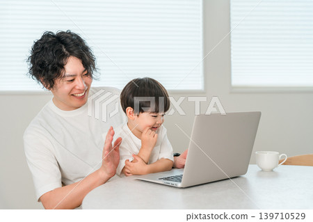 A parent and child waving while making a video call using a computer. A parent and child waving while making a video call using a computer. 139710529