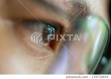 Macro closeup of human eye behind eyeglasses showing vision focus reflection detailed facial features Macro closeup of human eye behind eyeglasses showing vision focus reflection detailed facial features 139710644
