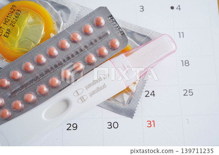 Pregnancy test with birth control pills and condom for female on calendar, ovulation day. Pregnancy test with birth control pills and condom for female on calendar, ovulation day. 139711235
