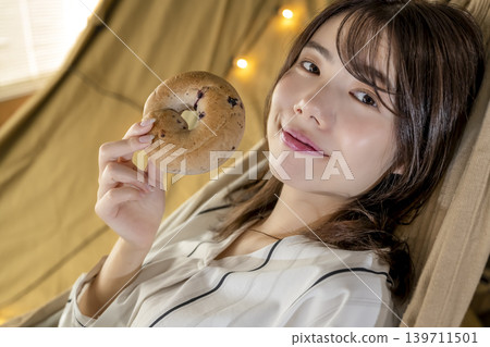 A young woman enjoying a bagel in her tent during her camping trip. A young woman enjoying a bagel in her tent during her camping trip. 139711501
