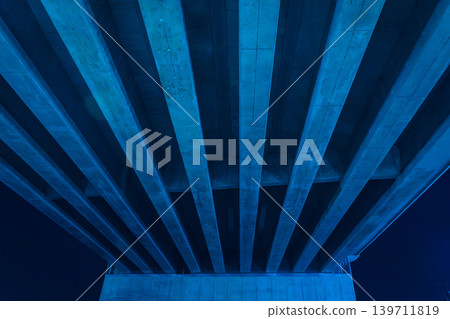 The geometric landscape of the concrete overpass and urban infrastructure at night, illuminated by blue light. The geometric landscape of the concrete overpass and urban infrastructure at night, illuminated by blue light. 139711819