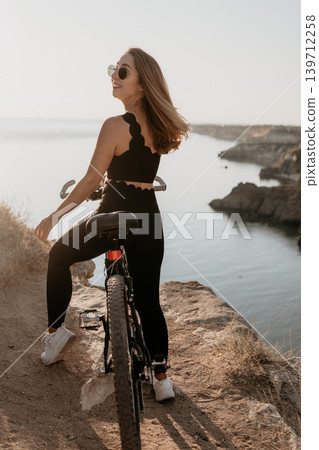 Woman bicycle cliff overlooks the calm sea as a female cyclist enjoys the scenic coastal landscape during a beautiful sunset trip 139712258