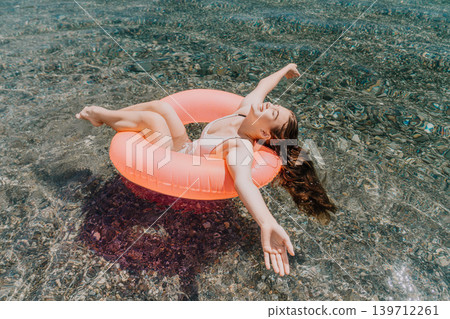 Woman floating sea enjoying summer vacation while relaxing on pink inflatable ring in clear turquoise water Woman floating sea enjoying summer vacation while relaxing on pink inflatable ring in clear turquoise water 139712261