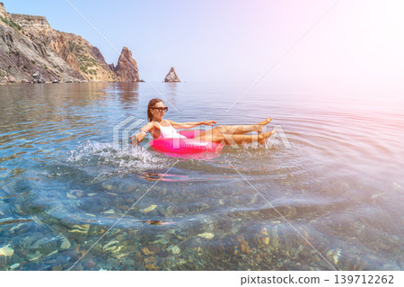 Woman floating ocean enjoying a peaceful summer vacation while relaxing on a pink inflatable ring in the crystal clear sea Woman floating ocean enjoying a peaceful summer vacation while relaxing on a pink inflatable ring in the crystal clear sea 139712262