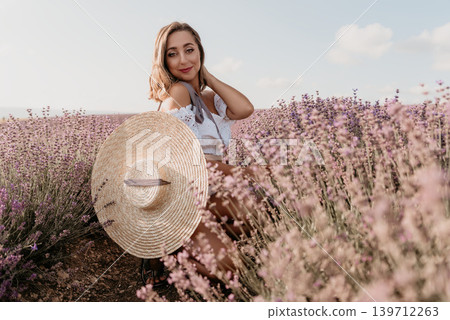 Lavender woman hat posing in a purple flower field during summer for a peaceful nature and travel concept Lavender woman hat posing in a purple flower field during summer for a peaceful nature and travel concept 139712263