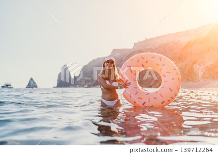 Woman, sea, donut float. Young woman with inflatable donut enjoys summer vacation at scenic beach with copy space. 139712264